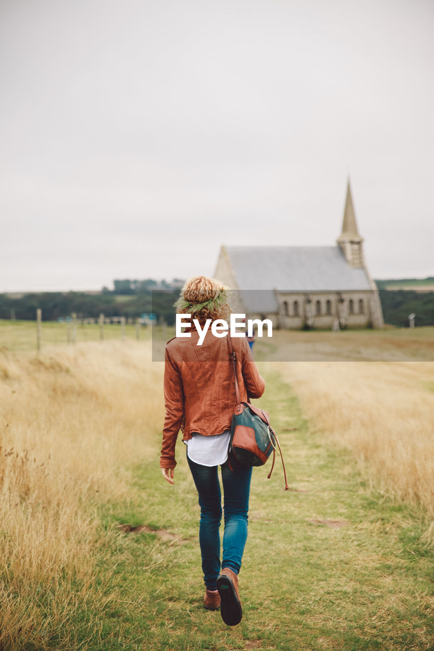 Rear view of woman walking on field against sky