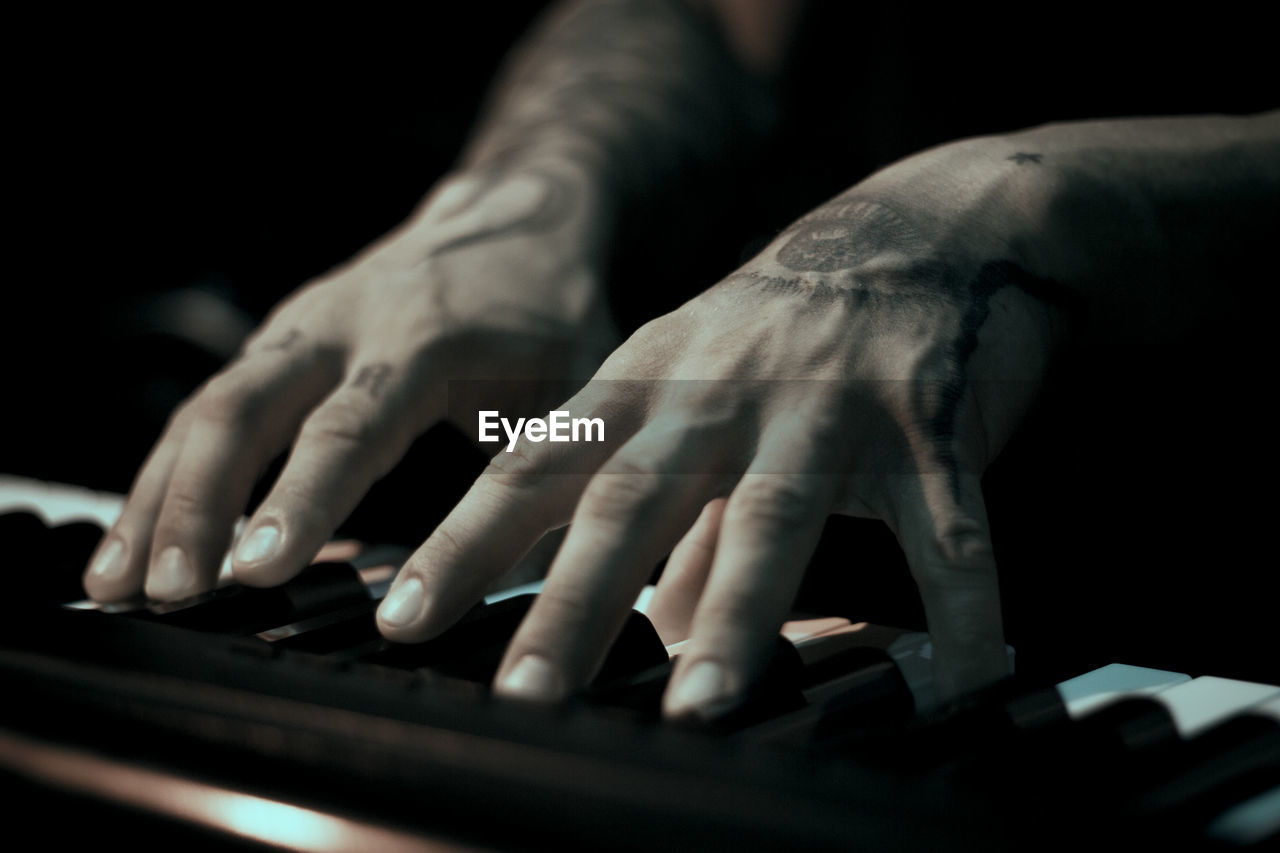 Tattooed mans hands on the keyboard of a piano. dark background