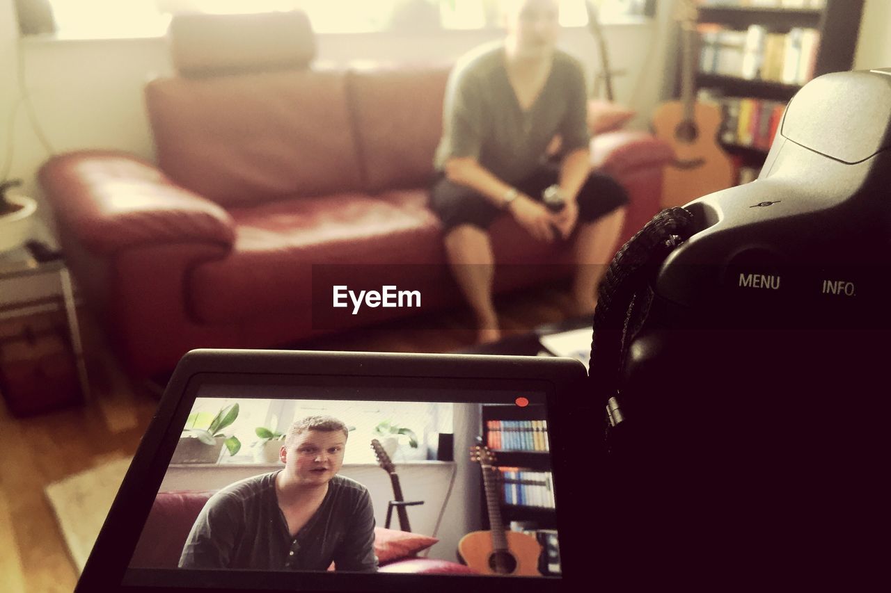 Close-up of camera filming man sitting on sofa at home