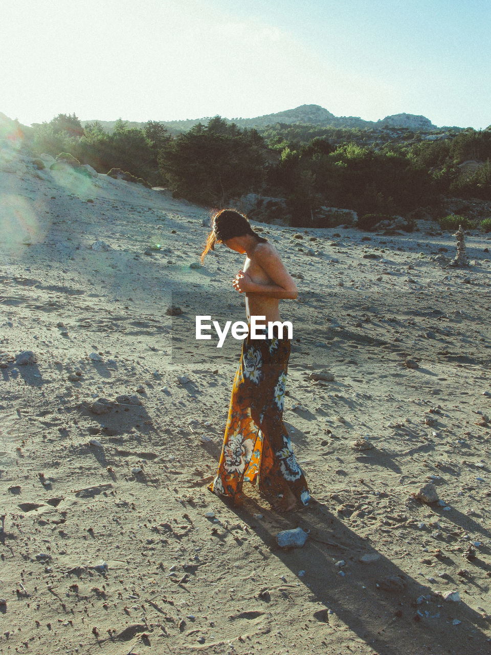 Side view of shirtless woman standing against sky