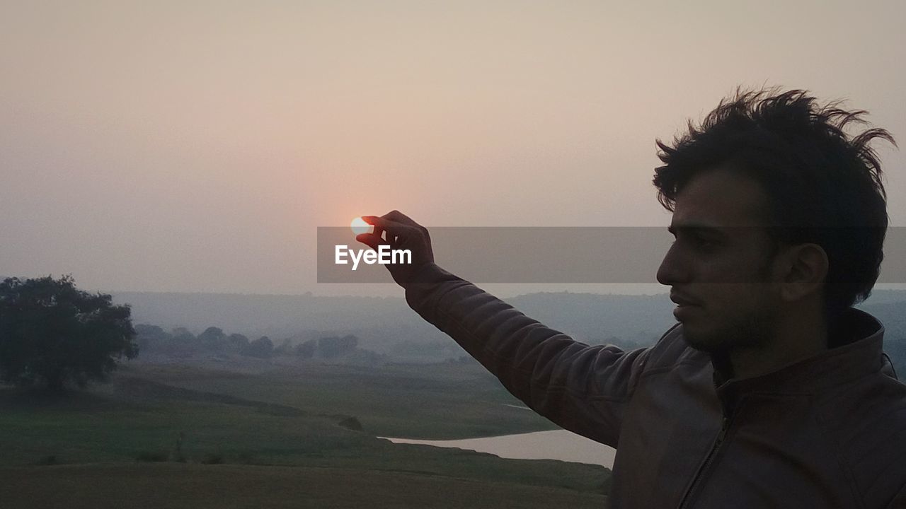 Optical illusion of man holding sun against clear sky during sunset