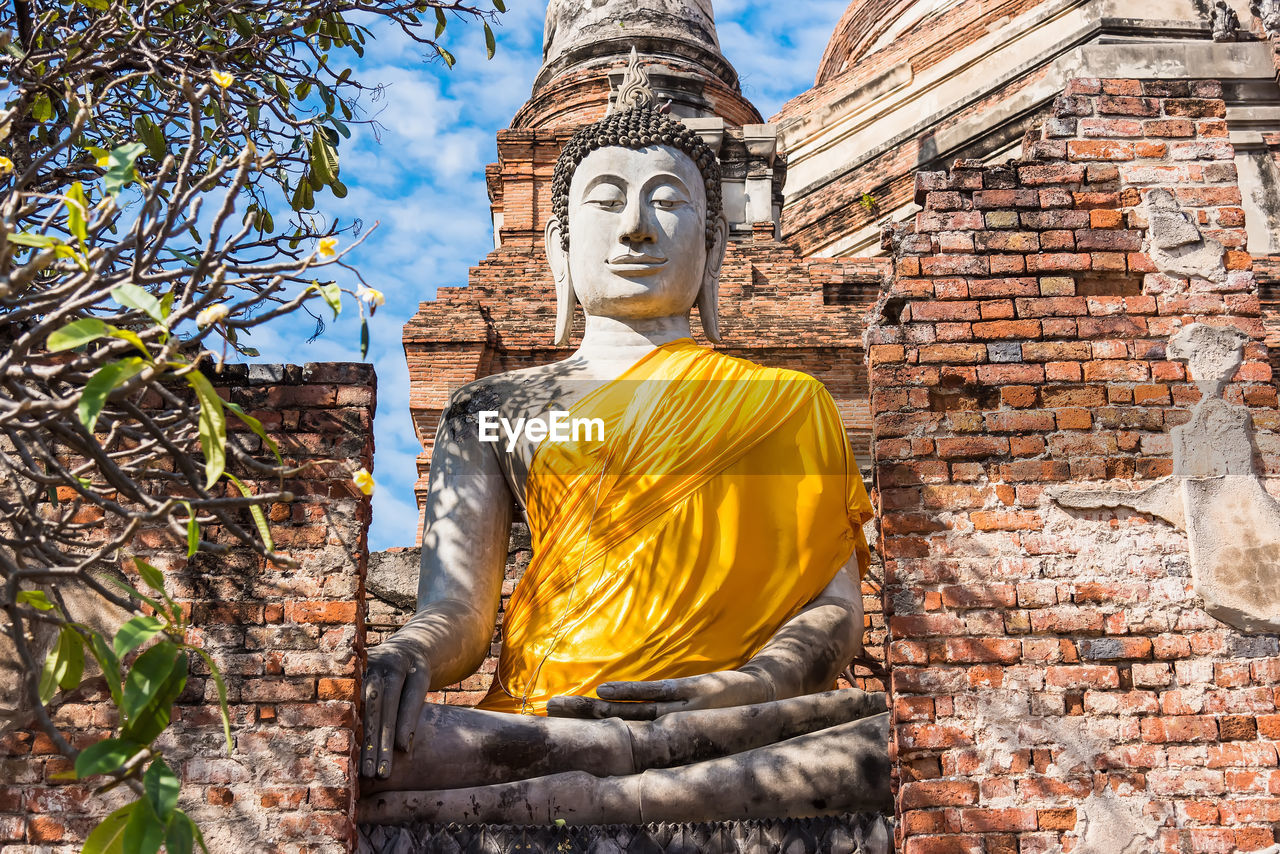 LOW ANGLE VIEW OF STATUE AGAINST TEMPLE BUILDING AGAINST BRICK WALL