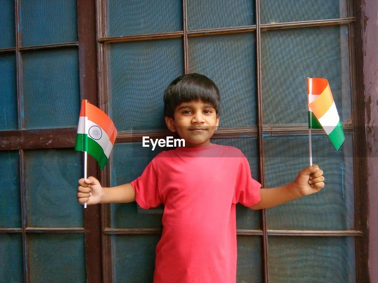 Portrait of boy holding indian flags against window