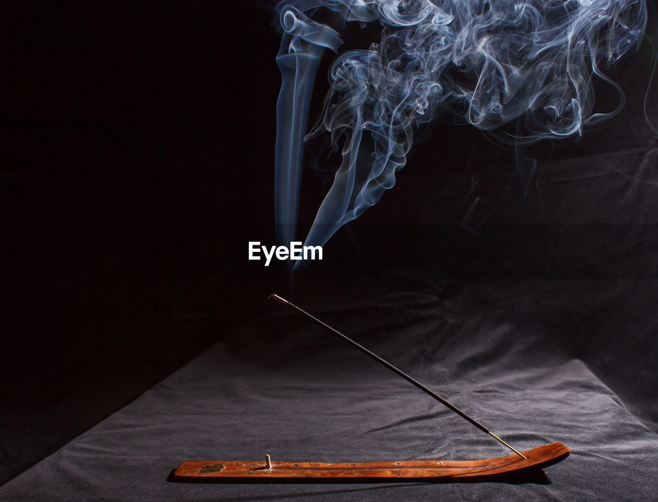 CLOSE-UP OF SMOKE EMITTING FROM CIGARETTE ON TABLE AT NIGHT