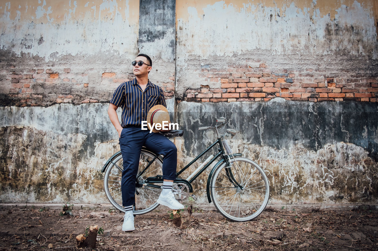 Full length of man sitting against wall on bicycle