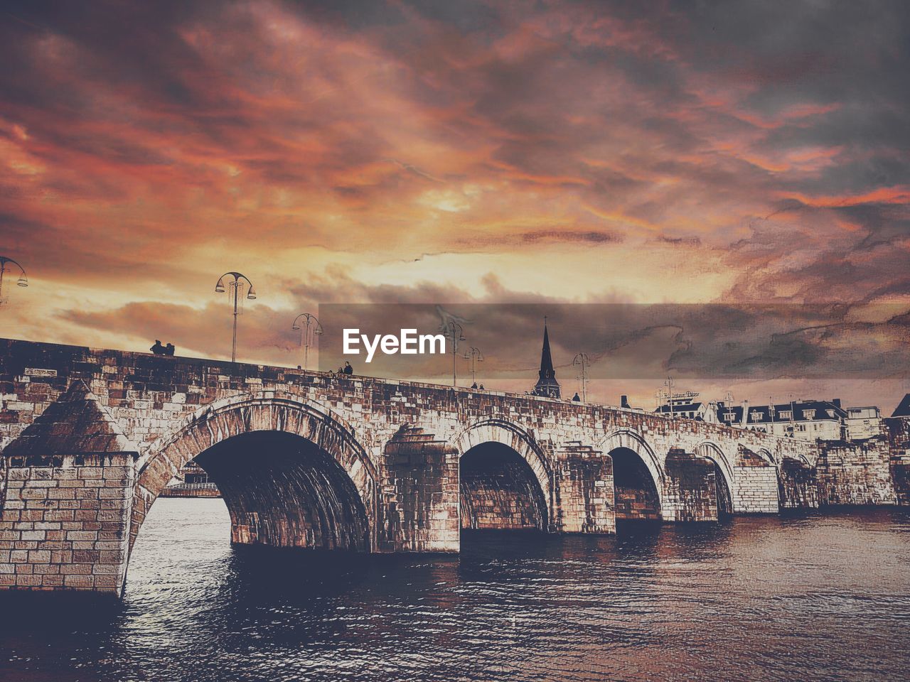 Bridge over river against cloudy sky during sunset