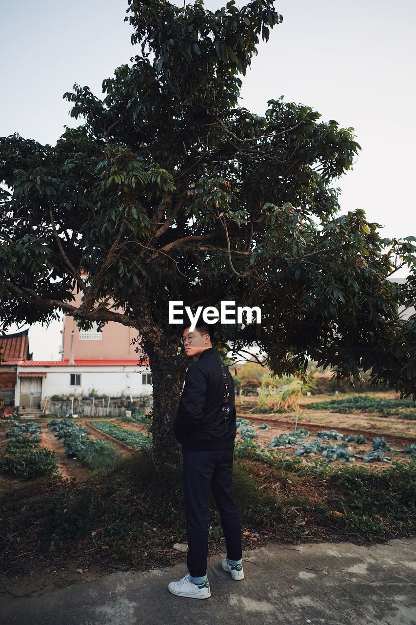 SIDE VIEW OF MAN STANDING BY TREE