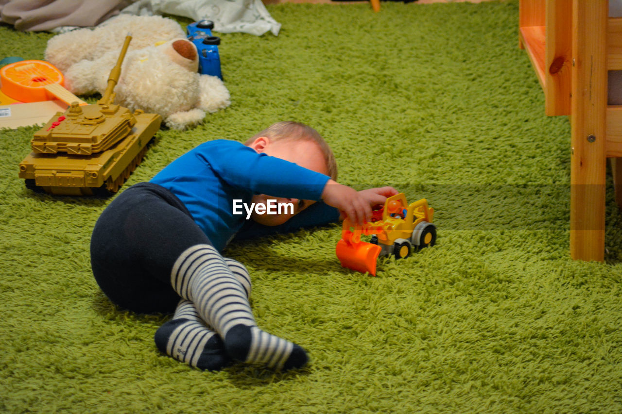 Baby boy playing with toy while lying on rug at home