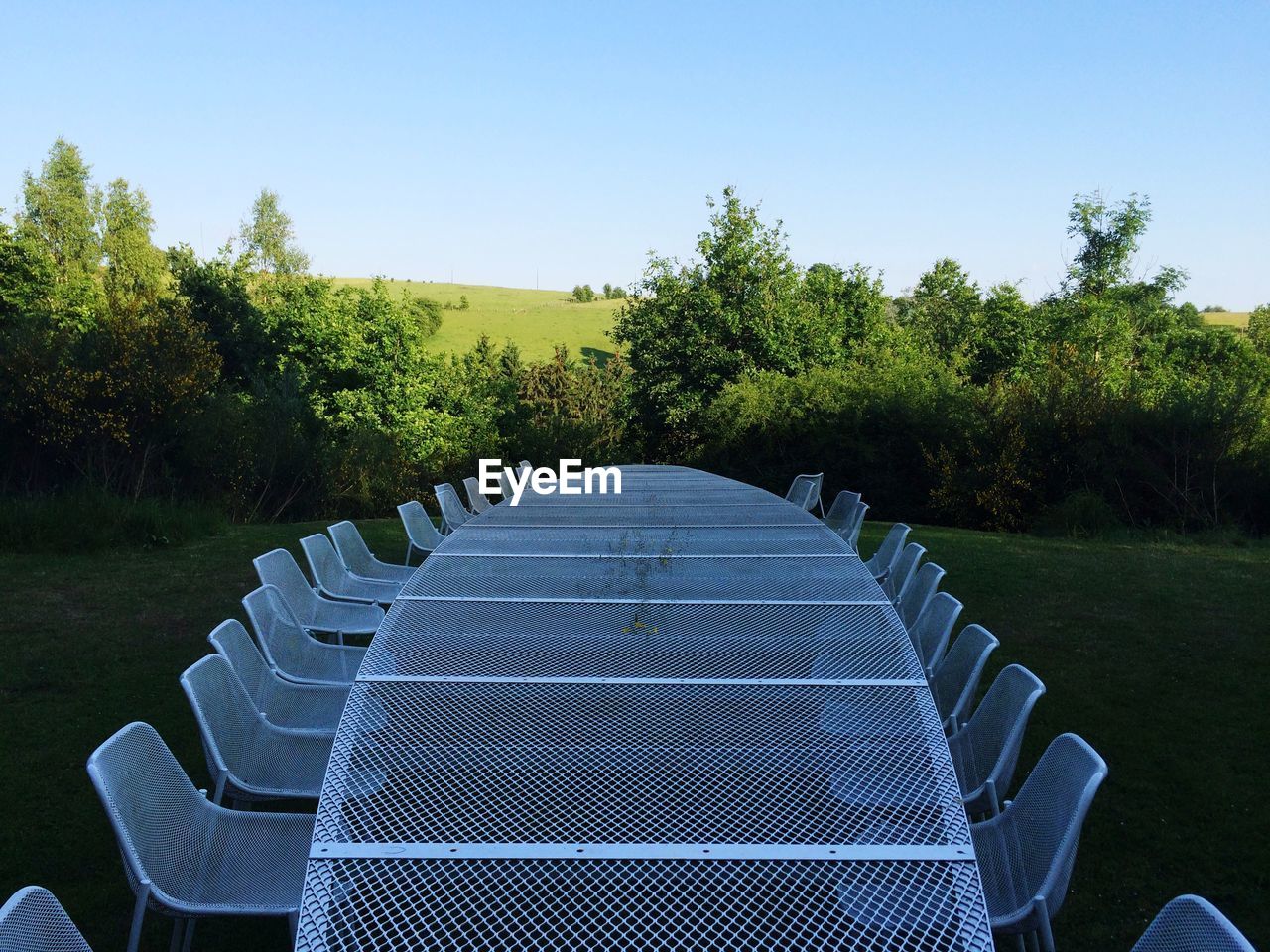 Empty metal chairs and table on field against clear sky