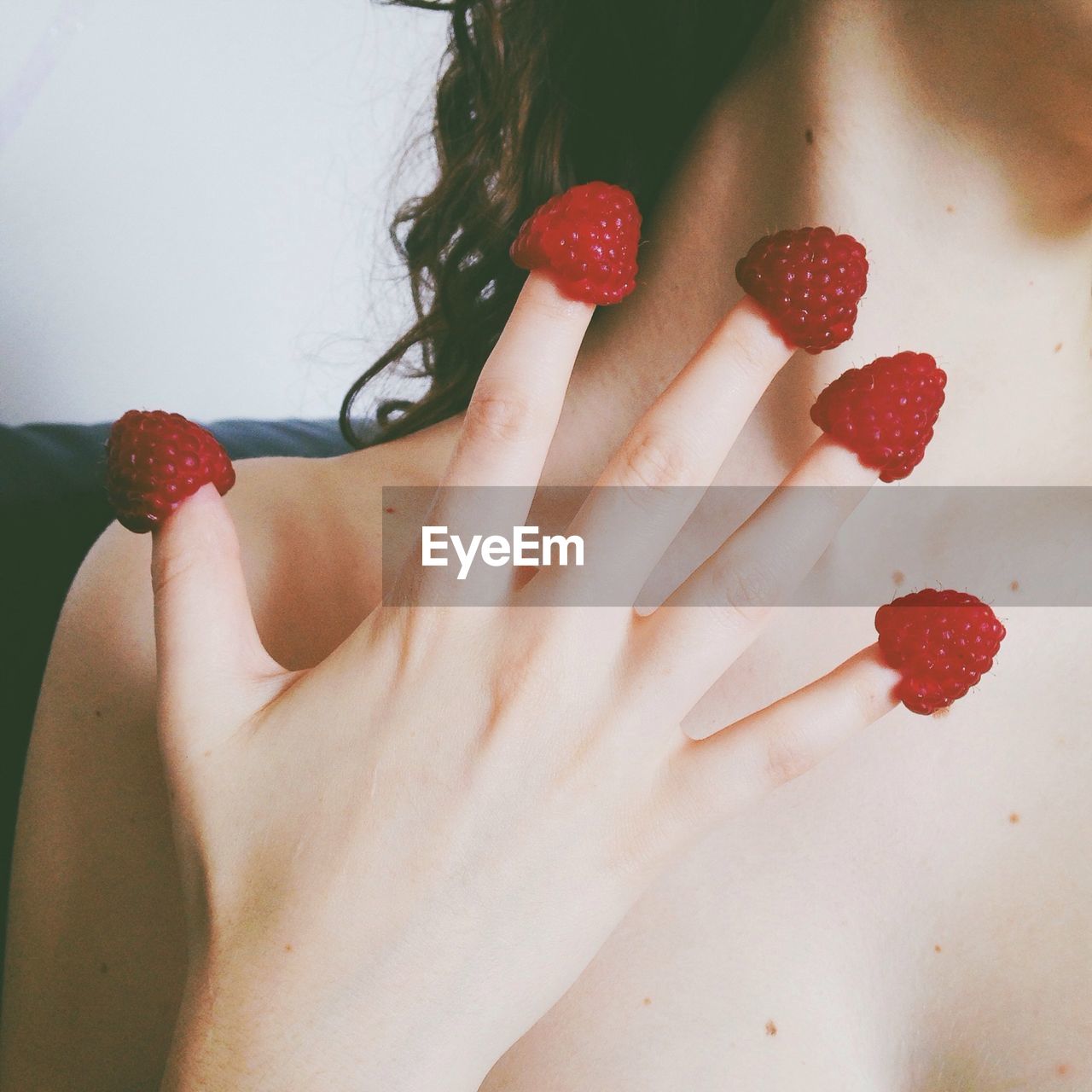 Close-up mid section of woman holding raspberries in fingers