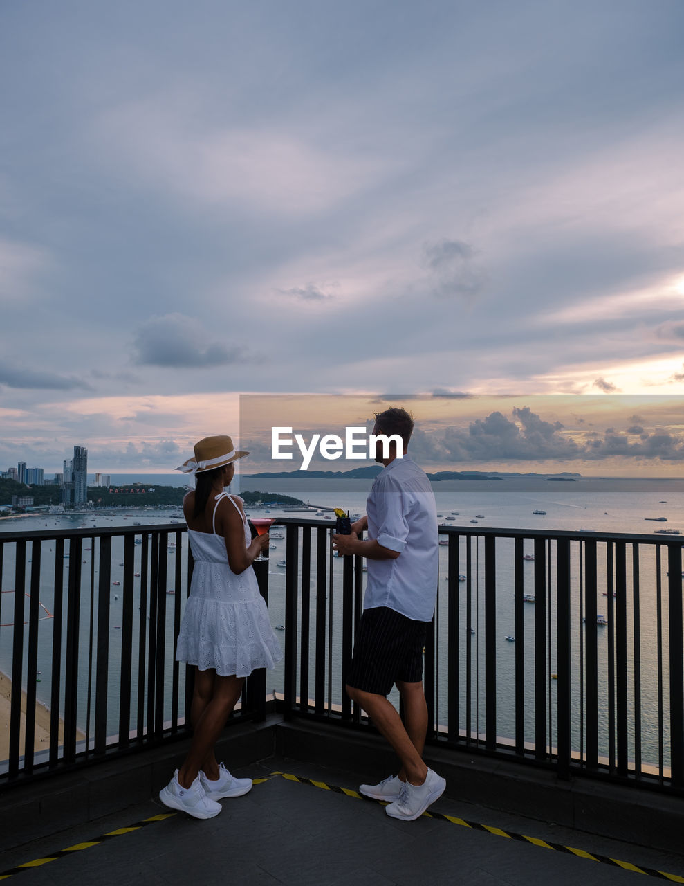 rear view of couple standing by railing against sea during sunset