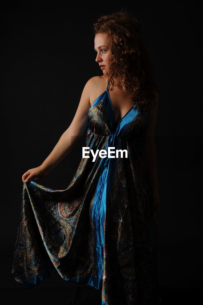 Woman looking away while standing against black background