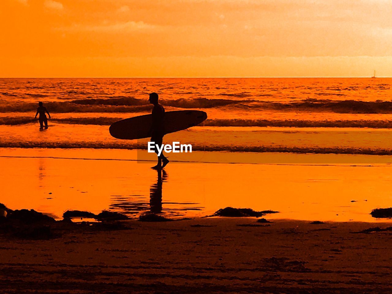 SILHOUETTE PEOPLE ON BEACH AGAINST ORANGE SKY