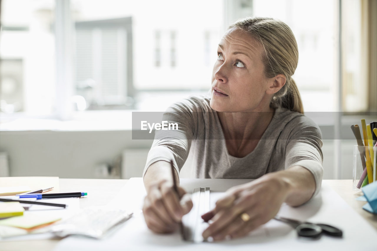 Businesswoman drawing line using ruler on paper while looking away