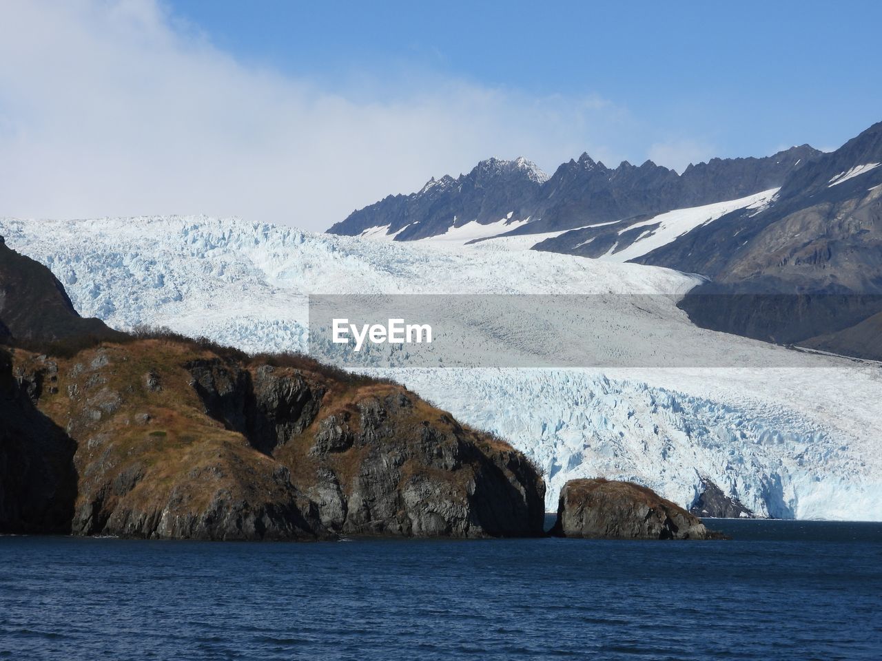 Scenic view of sea by mountain against sky