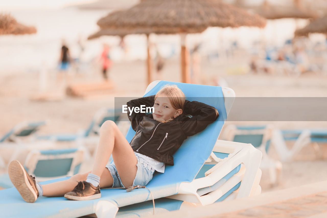 Full length portrait of smiling girl lying on lounge chair at beach