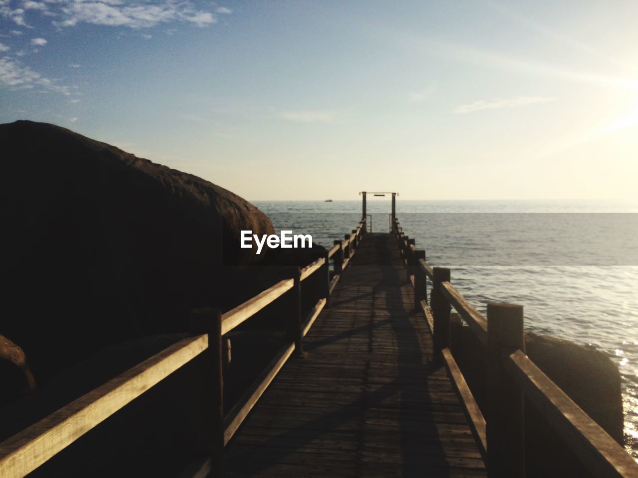 Jetty by boulders in sea against sky