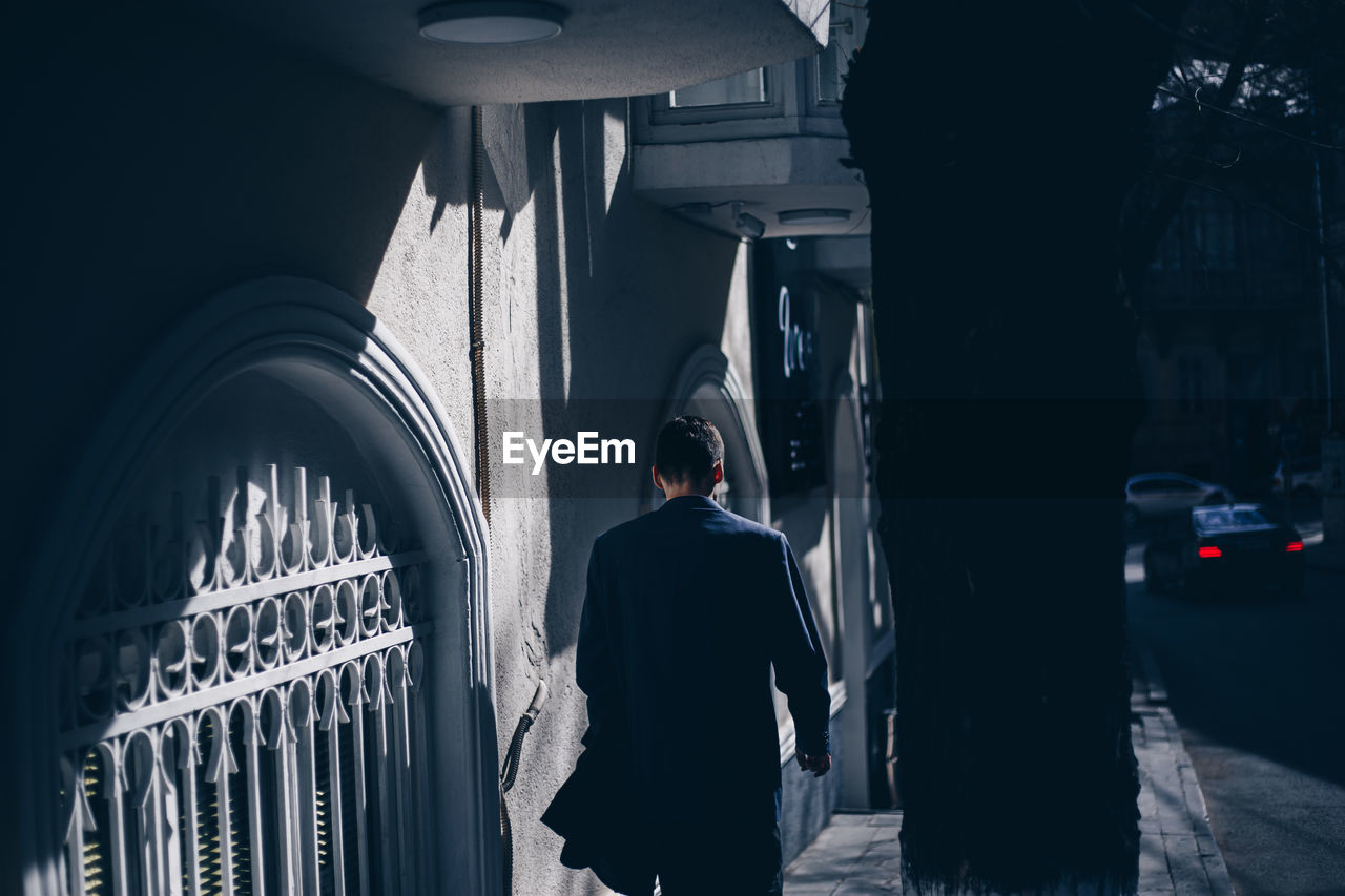 Rear view of man standing on street amidst buildings in city