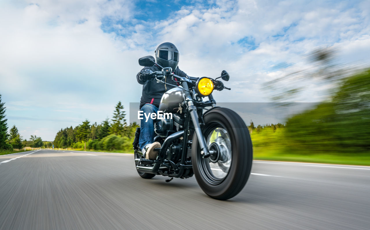 Man riding motorcycle on road against cloudy sky