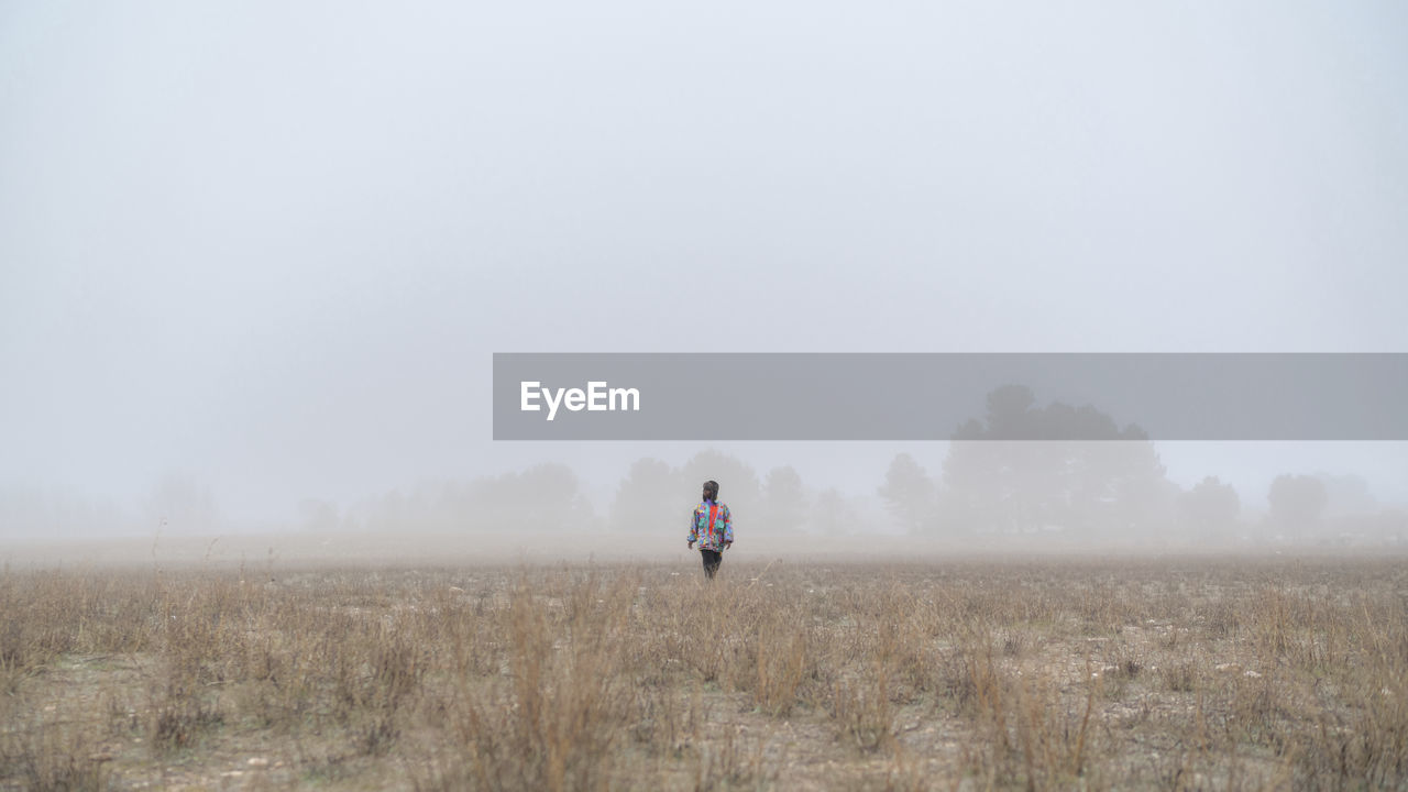 Person strolling on dry meadow against misty trees in nature in winter day person