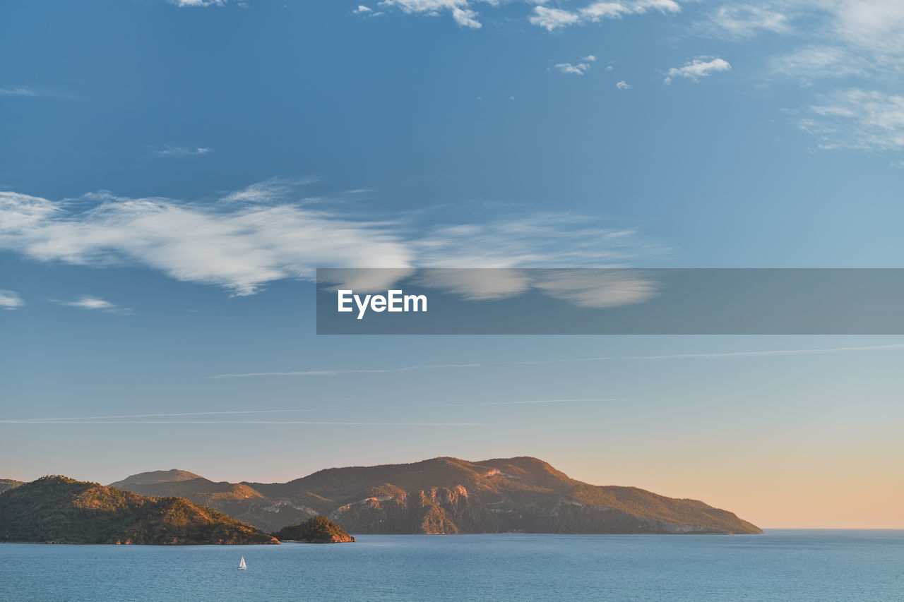 Beautiful sunset on the aegean sea with islands, mountains and a sailboat. 