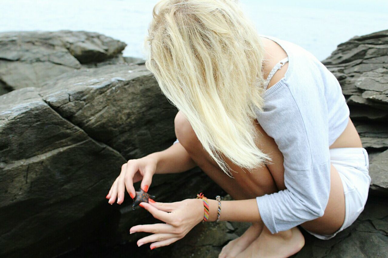 Side view of young woman holding starfish while sitting on rock formation