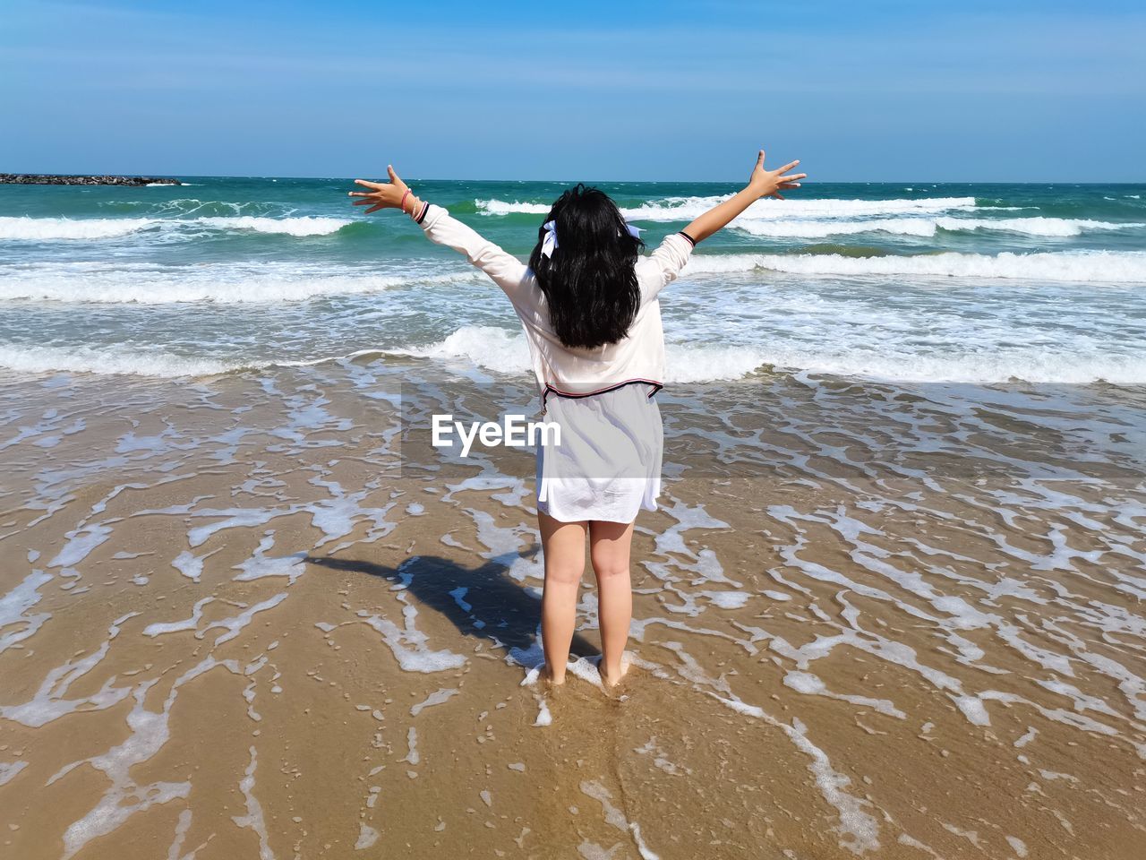 Rear view of young girlr with  arms raise standing on the beach looking at beautiful seascape 