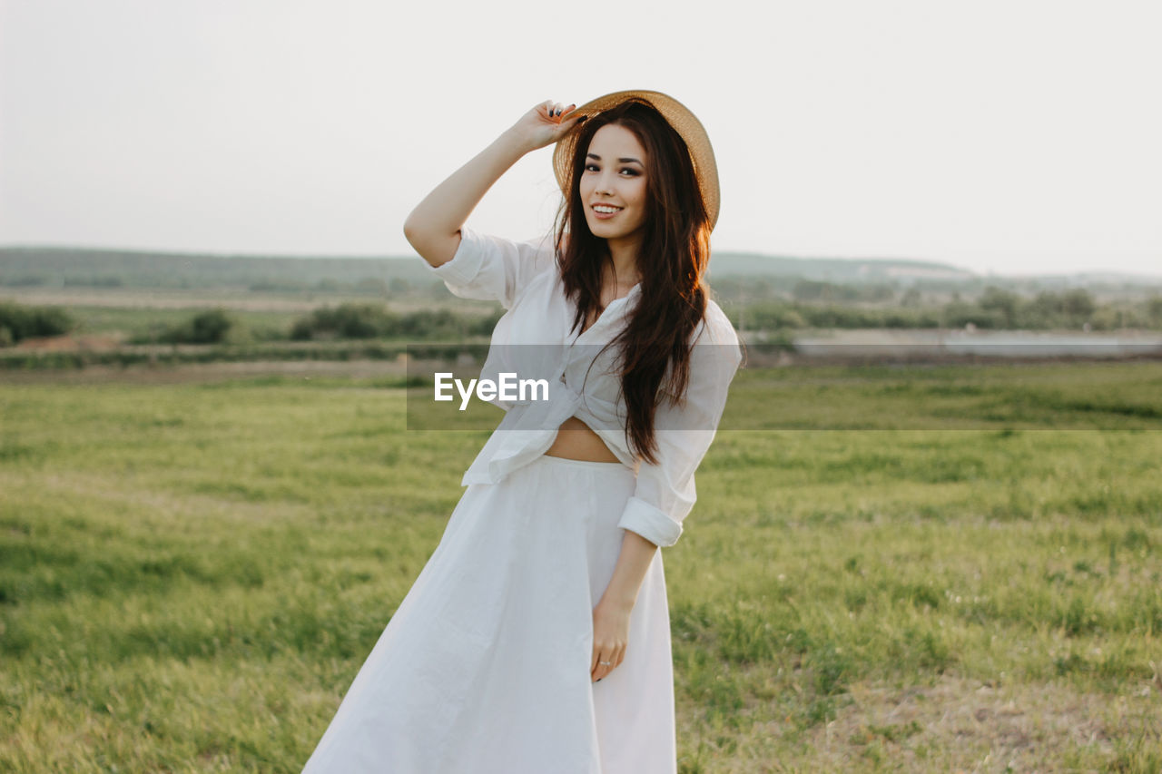 Portrait of woman standing on grass against sky