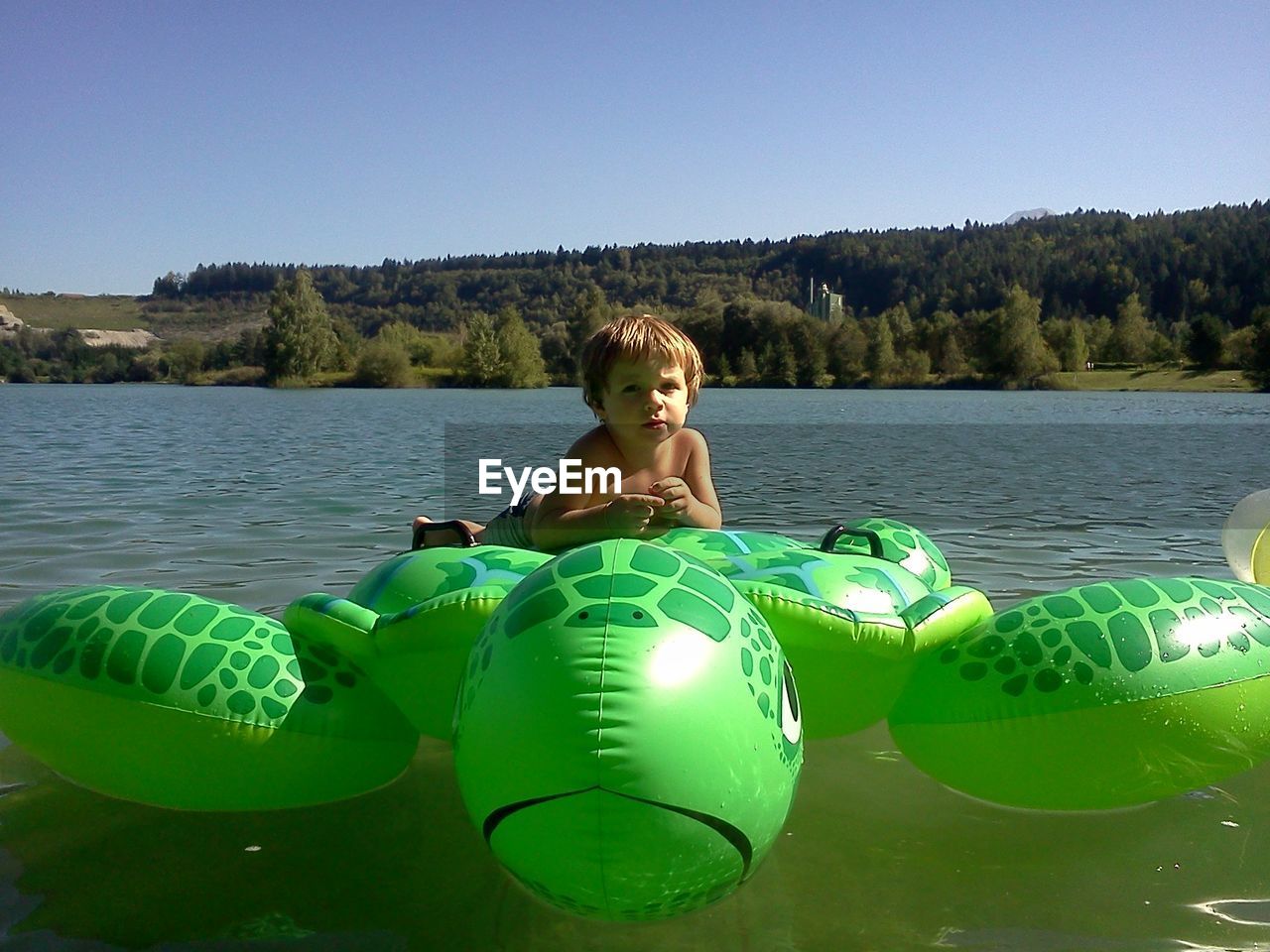 Portrait of boy relaxing on pool raft at lake against clear sky