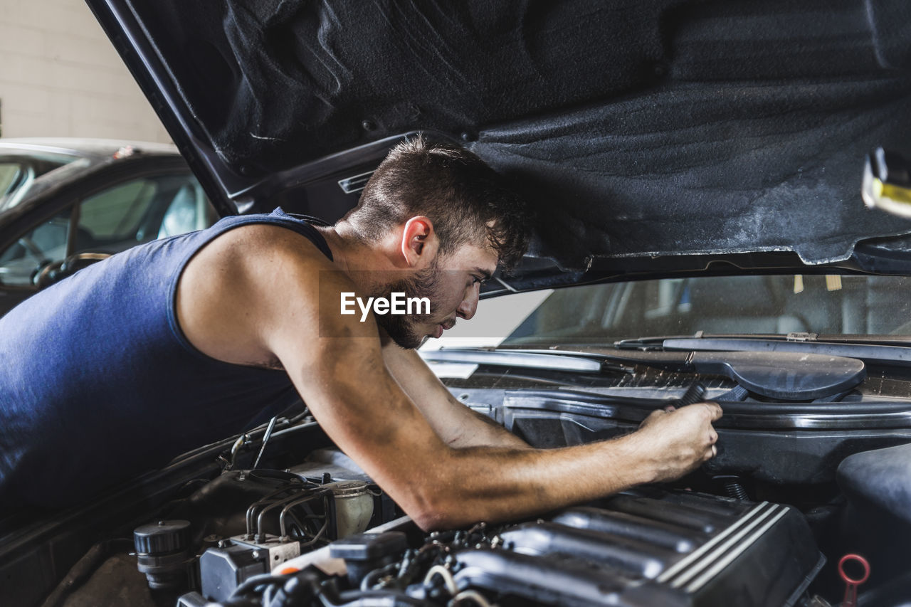 Side view of dirty man loosening screws on motor while fixing car in garage