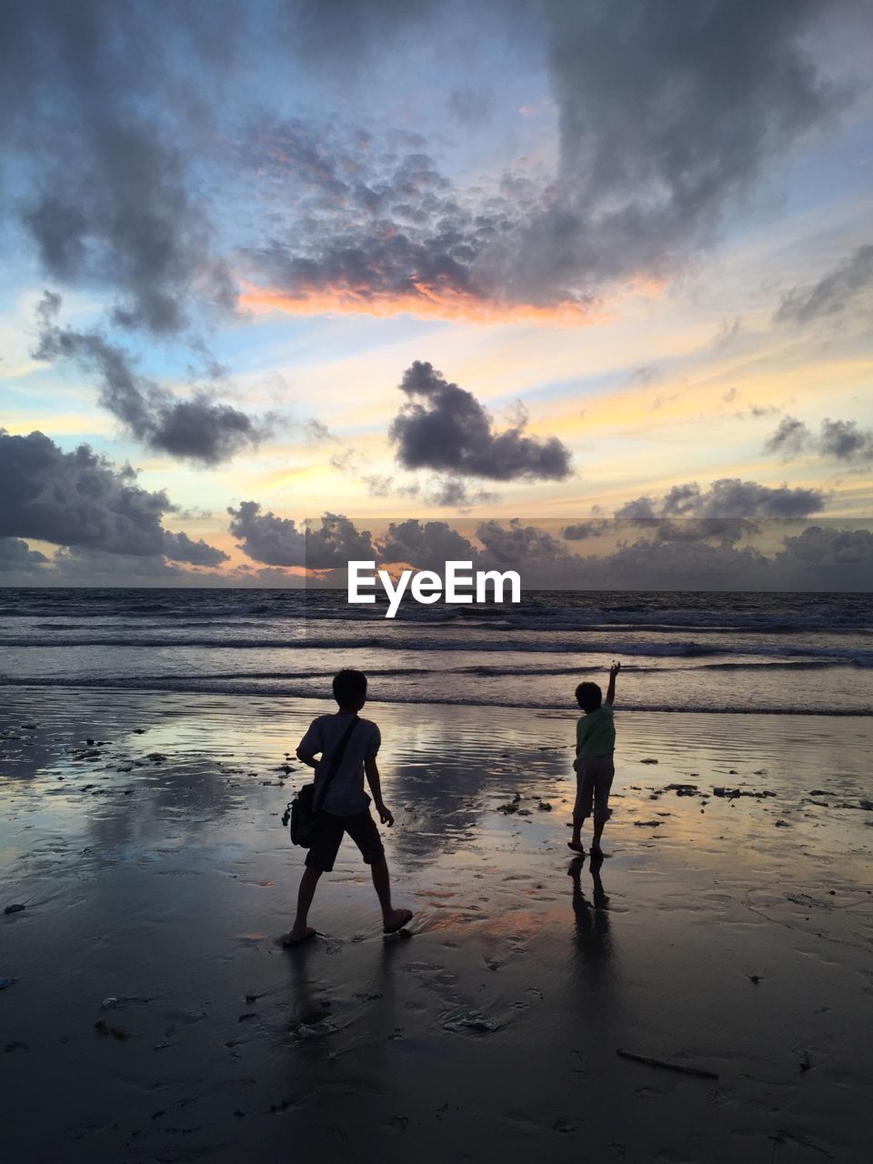 Silhouette boys enjoying at beach against cloudy sky at dusk