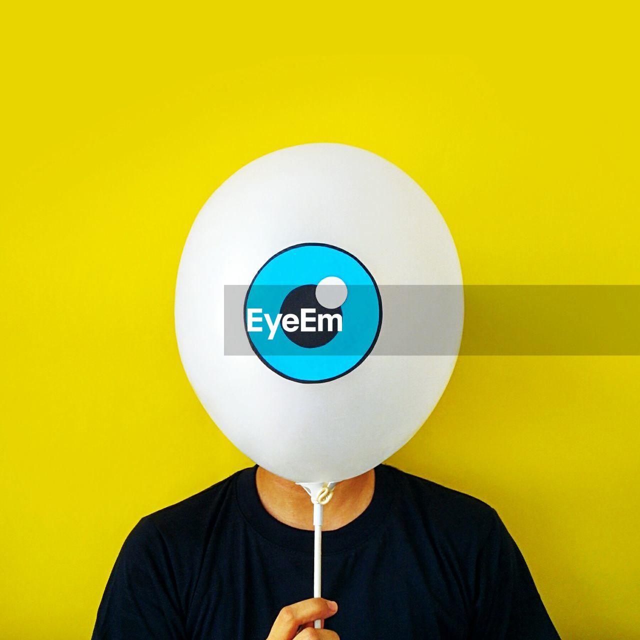 Man hiding face behind balloon against yellow background