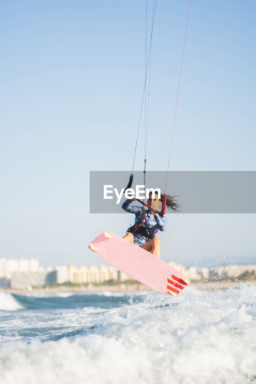 Female kite surfer in swimsuit ridding waves in sea on sunny day in summer