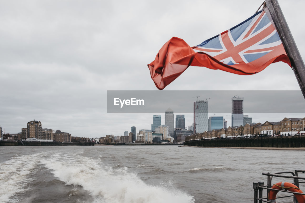 British flag waving on boat in river against sky