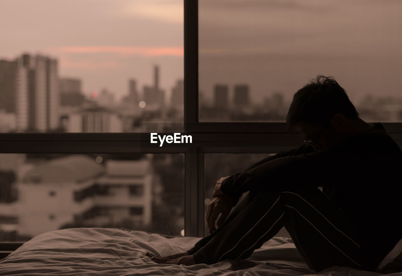 The man sitting on bed with city view from bedroom. stay home, depression and loneliness concept.