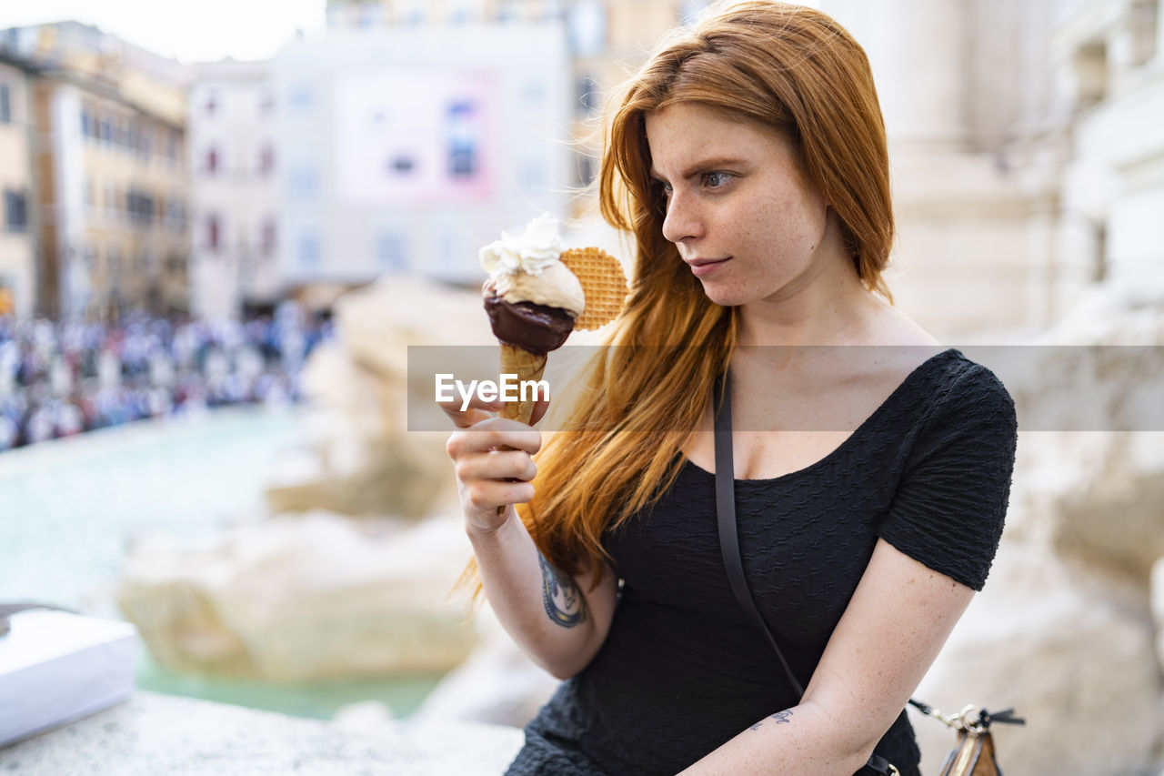 Young woman sitting on city street and eating ice cream