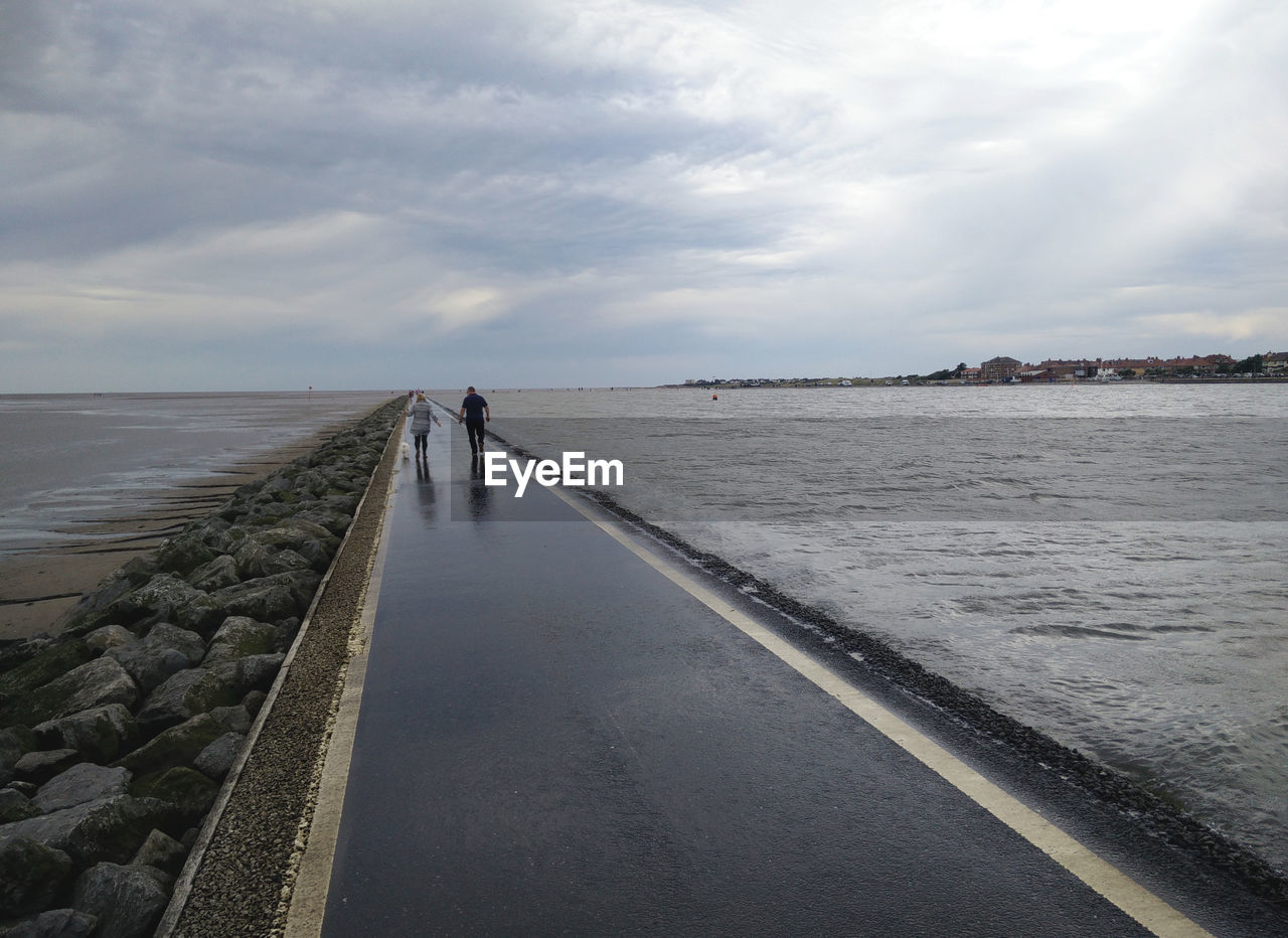 Rear view of people walking on road over sea against sky