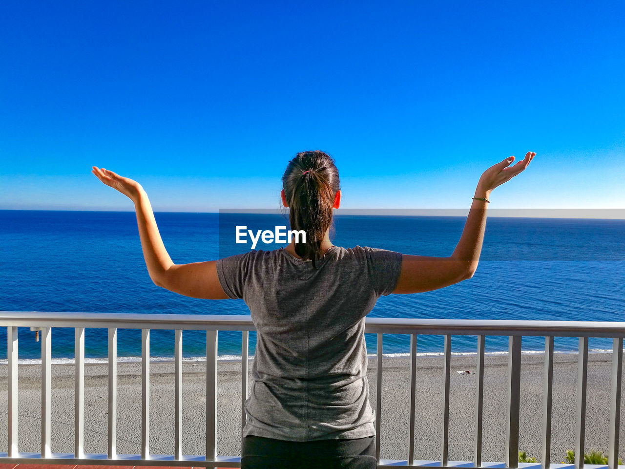 Rear view of woman with arms raised looking at sea against sky