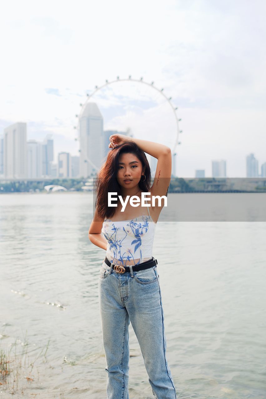 Fashionable young woman standing against sea and urban skyline