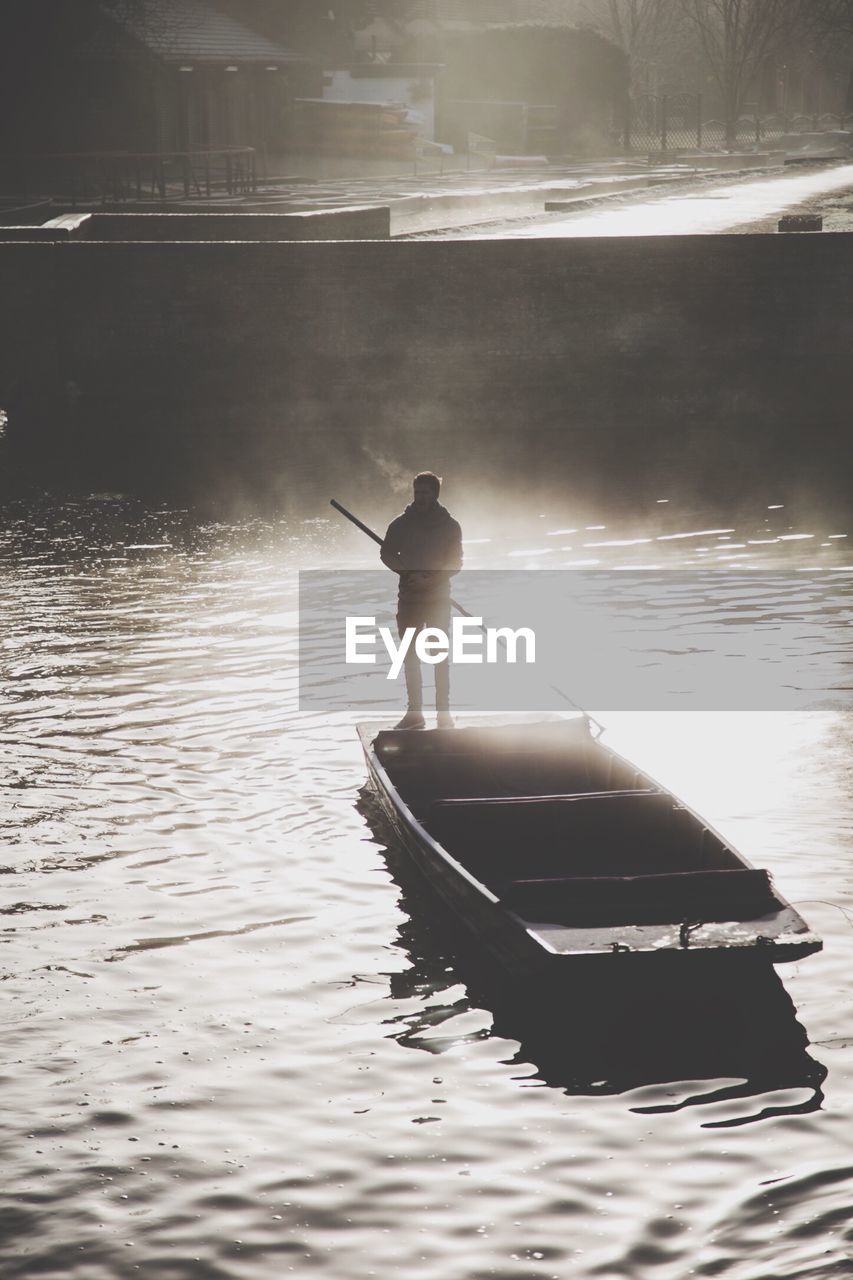 REAR VIEW OF MAN ON BOAT AT SHORE