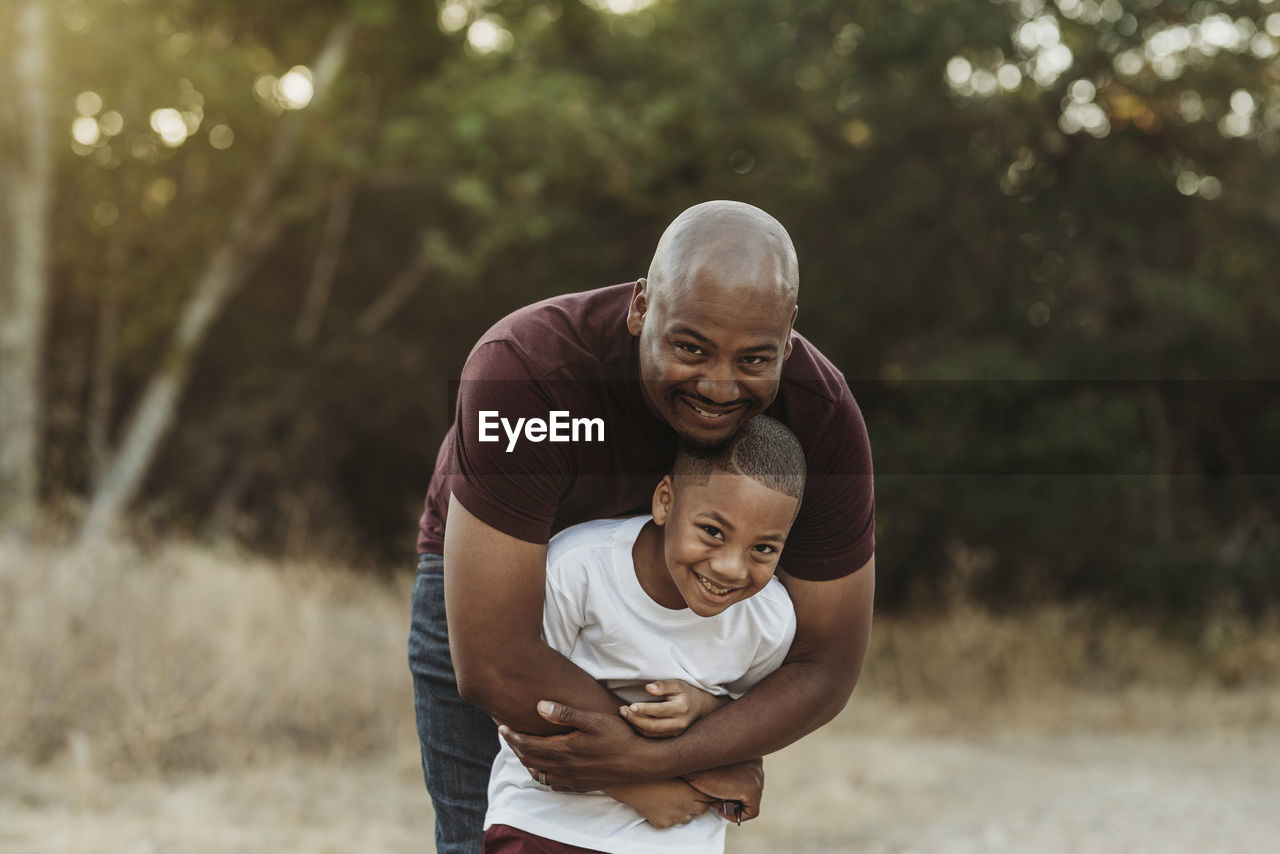 Close up of happy father and son hugging in backlit field