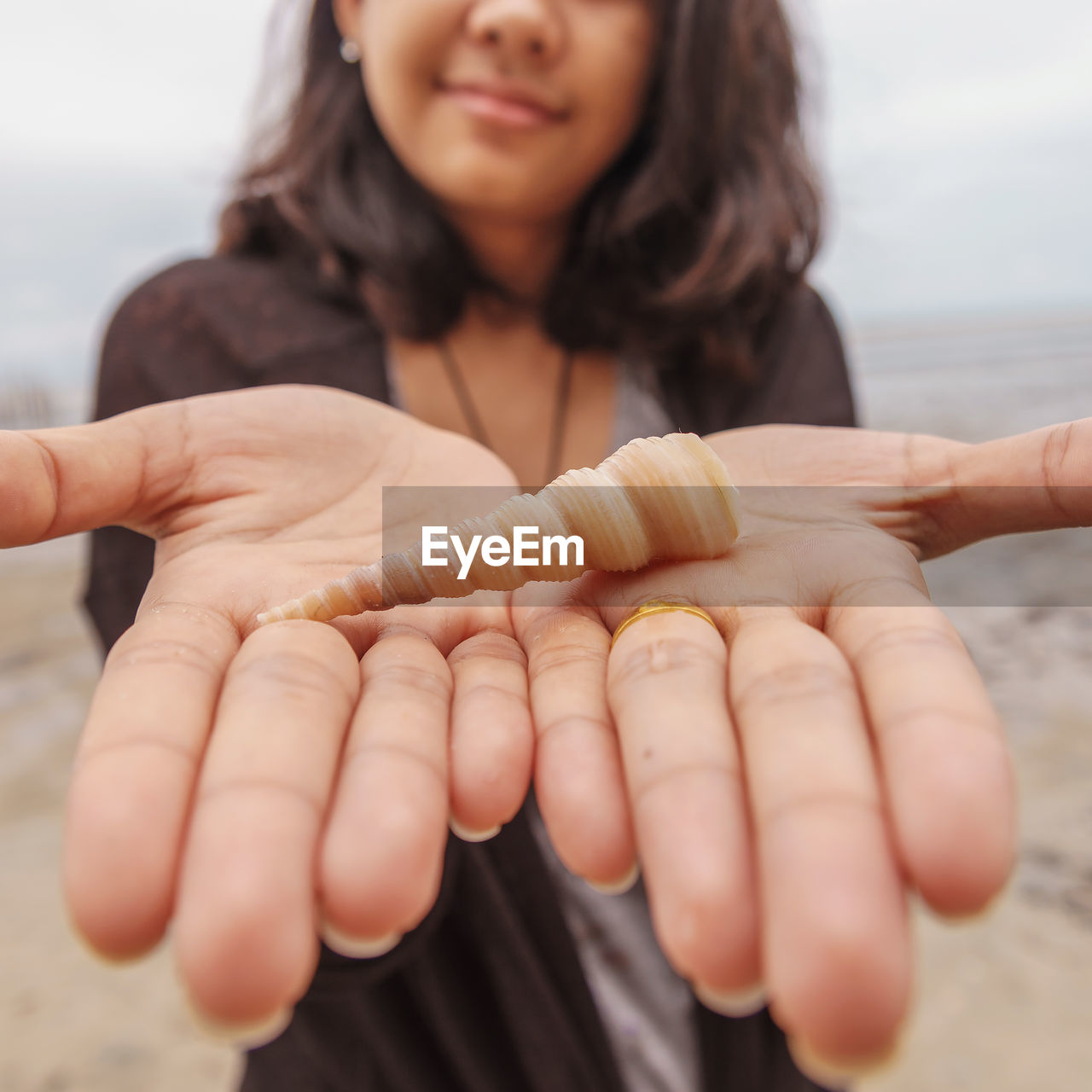 Midsection of girl showing shell while standing at beach