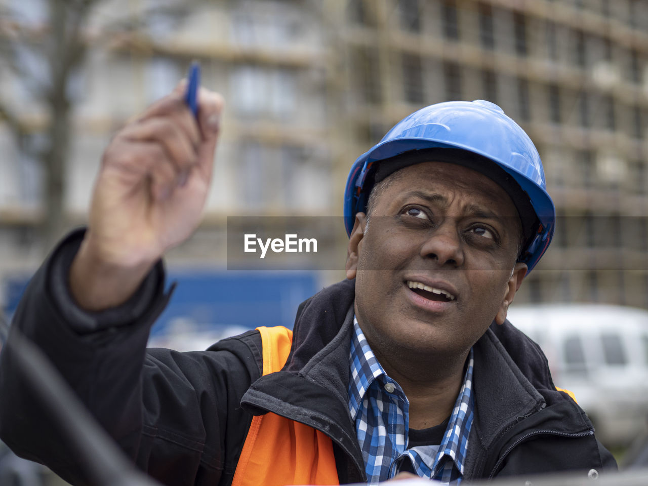 Indian architect wearing hardhat and a safety jacket pointing at something above him