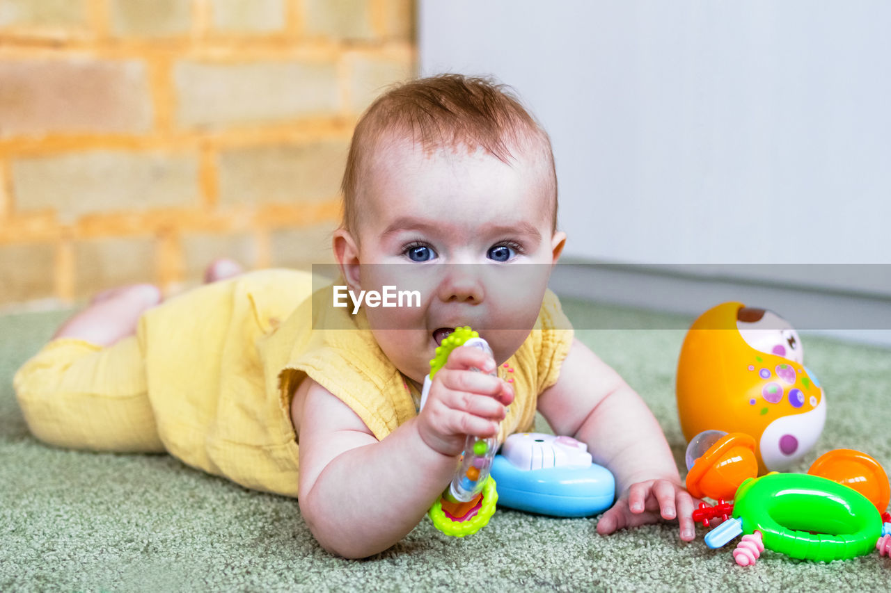 Little baby girl lying on a floor and playing with colorful toys. develop of child motor skills.