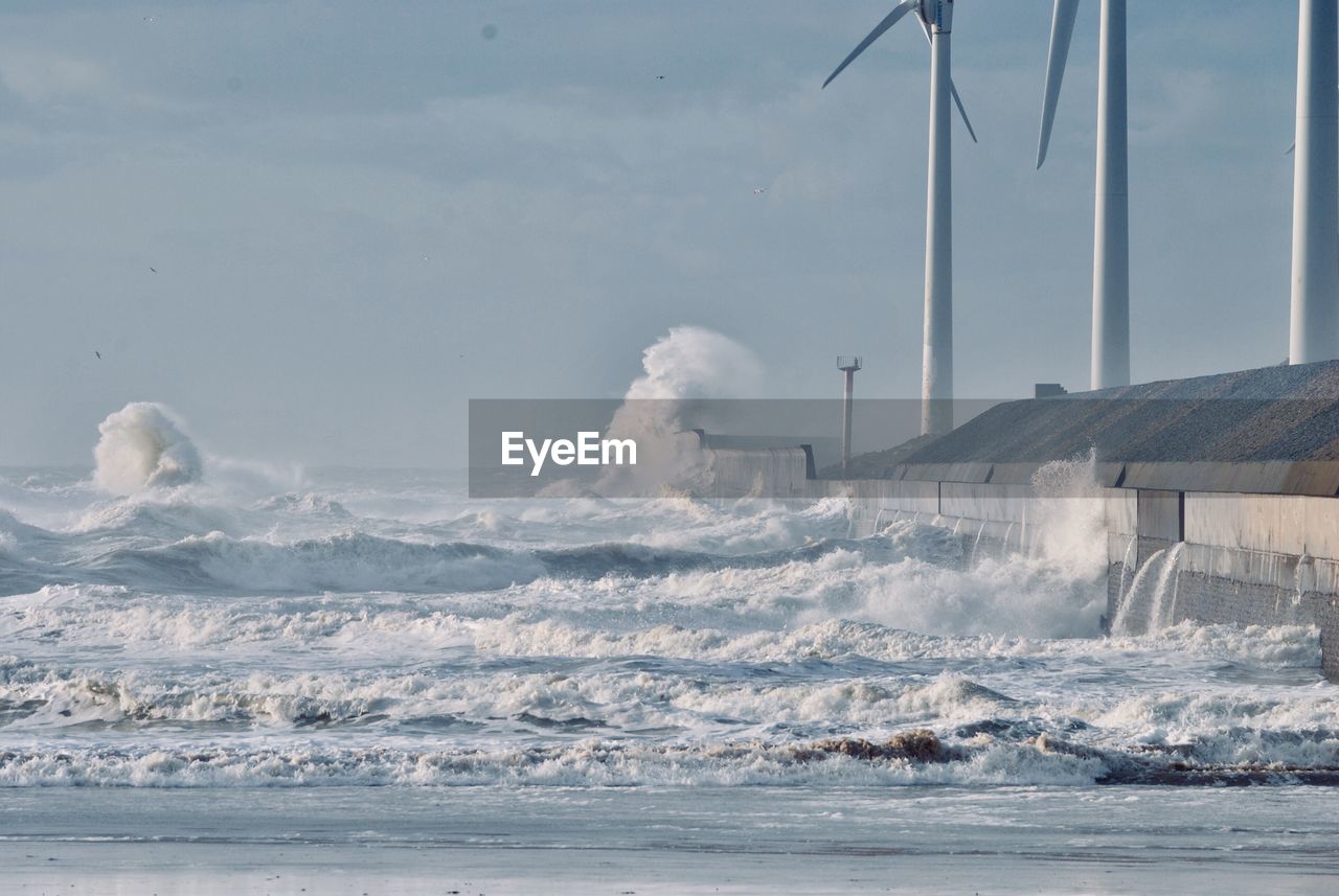 Sea waves splashing on shore against sky