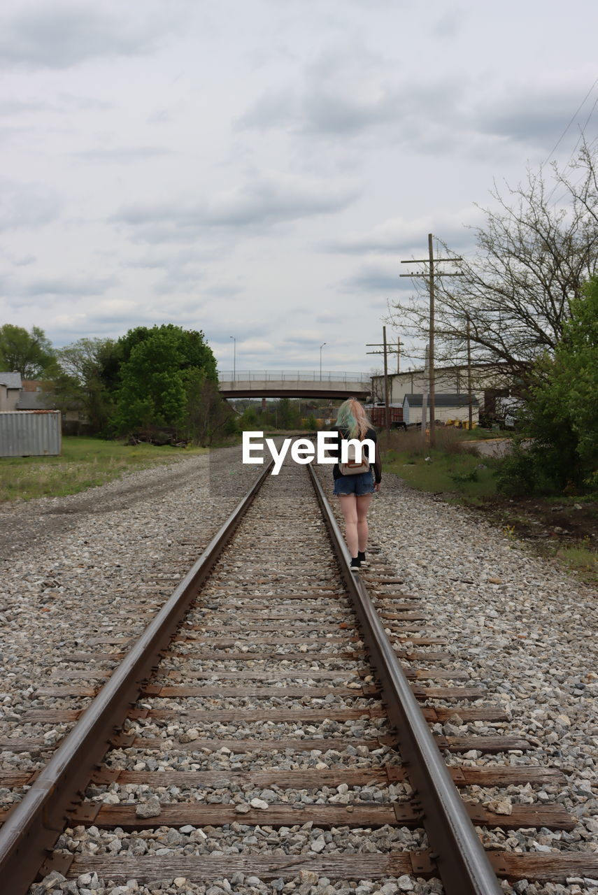 REAR VIEW OF MAN WALKING ON RAILROAD TRACKS