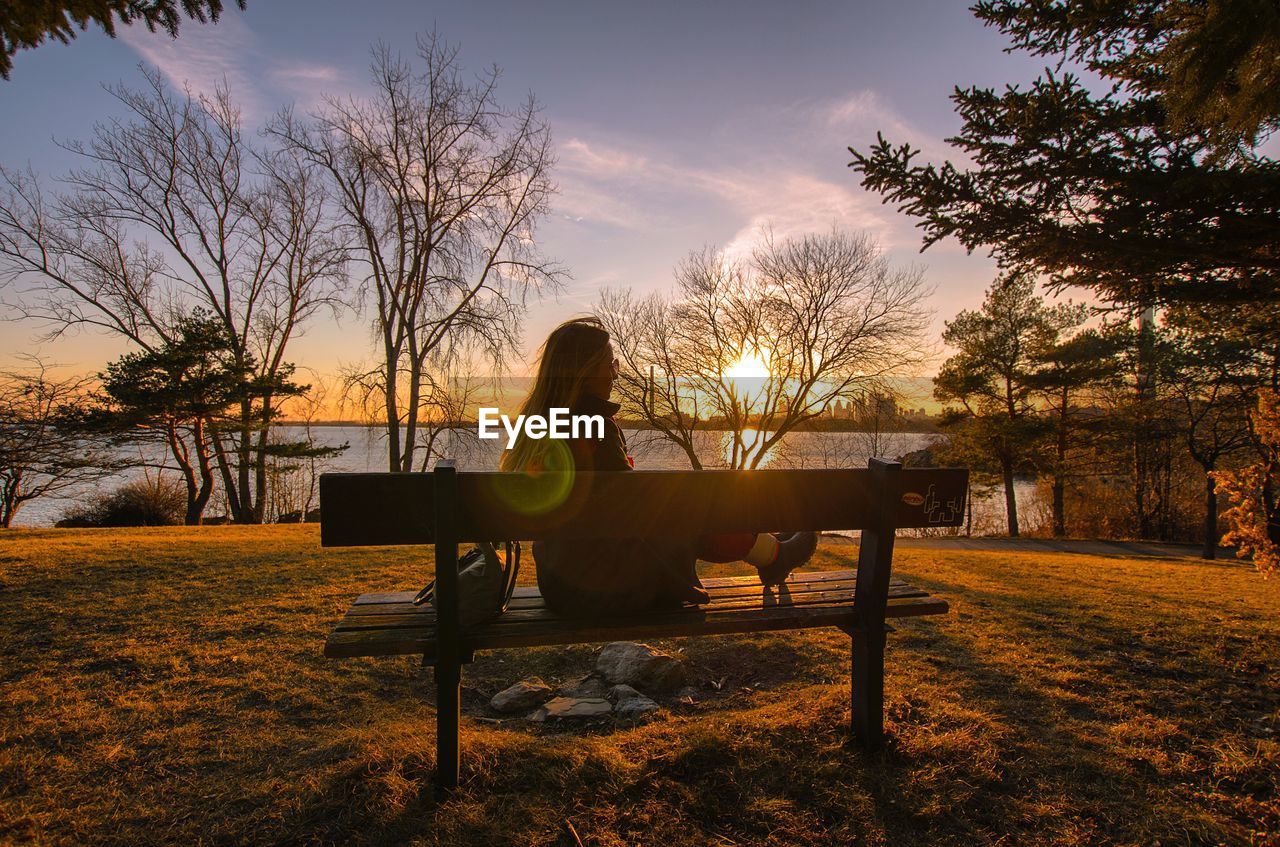 Silhouette woman sitting on bench in park during sunset