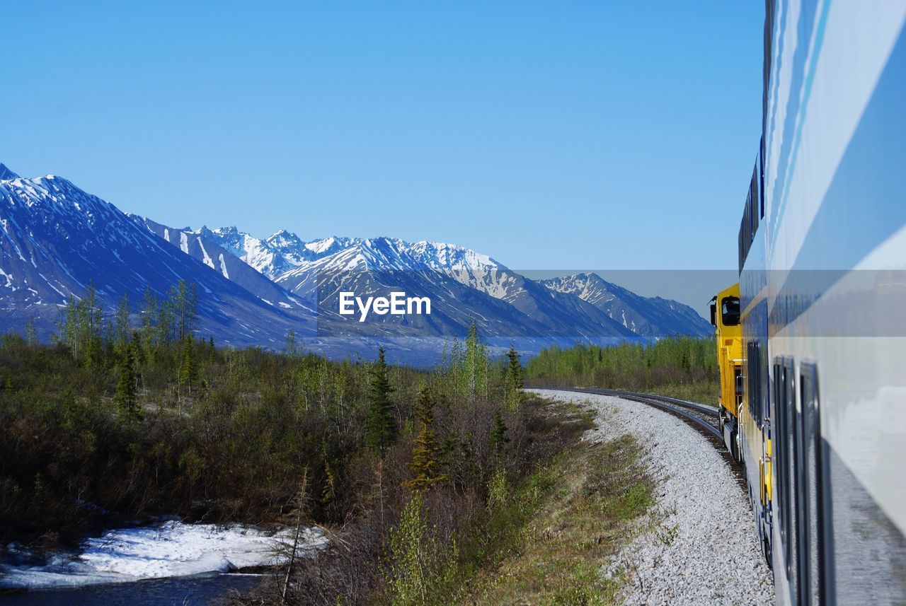 Train on railroad track against snowcapped mountains and clear sky