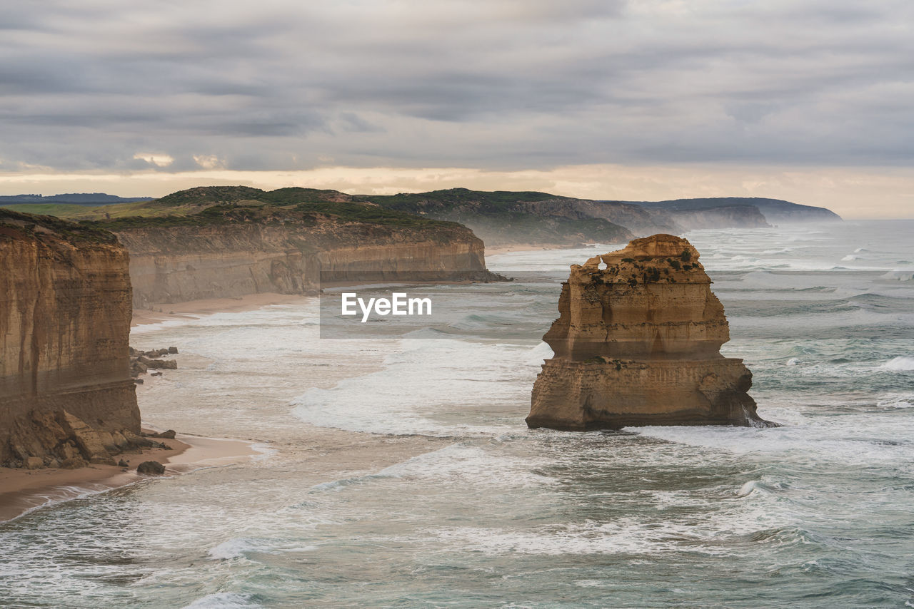 Moody scenery along great ocean road with rock formation on sea shore against sky