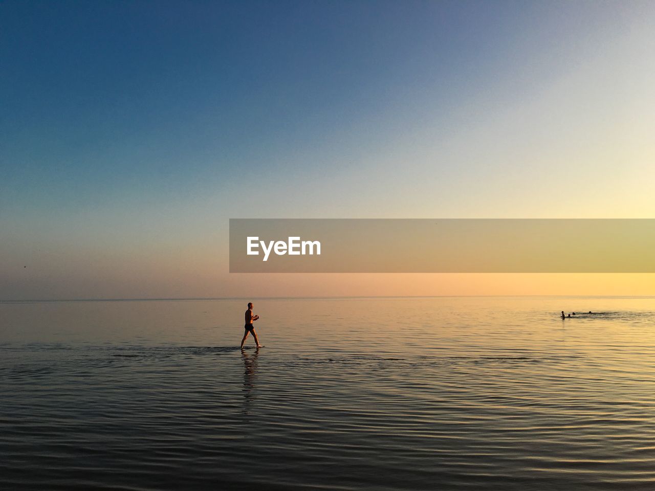 Mid distance of man walking in sea against sky during sunset